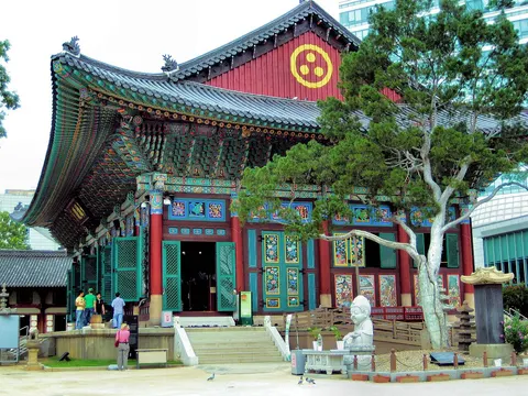 Jogyesa main hall with painted eaves, courtyard tree and city buildings behind